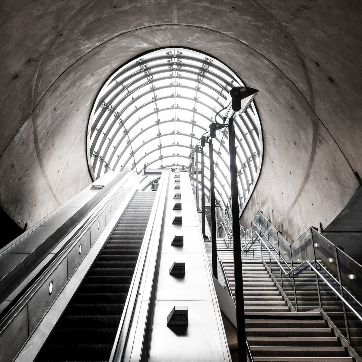 Escalator and stairs leading up a train station tunnel into the light