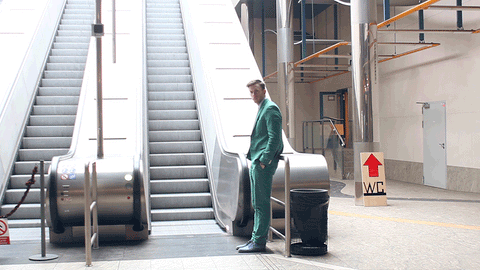 Man in green suit waiting by a moving empty clear escalator
