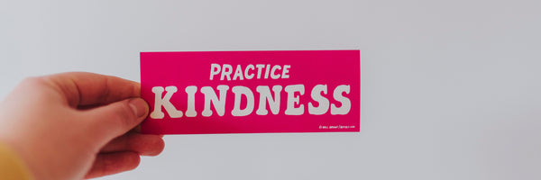 person holding a card that says practice kindness